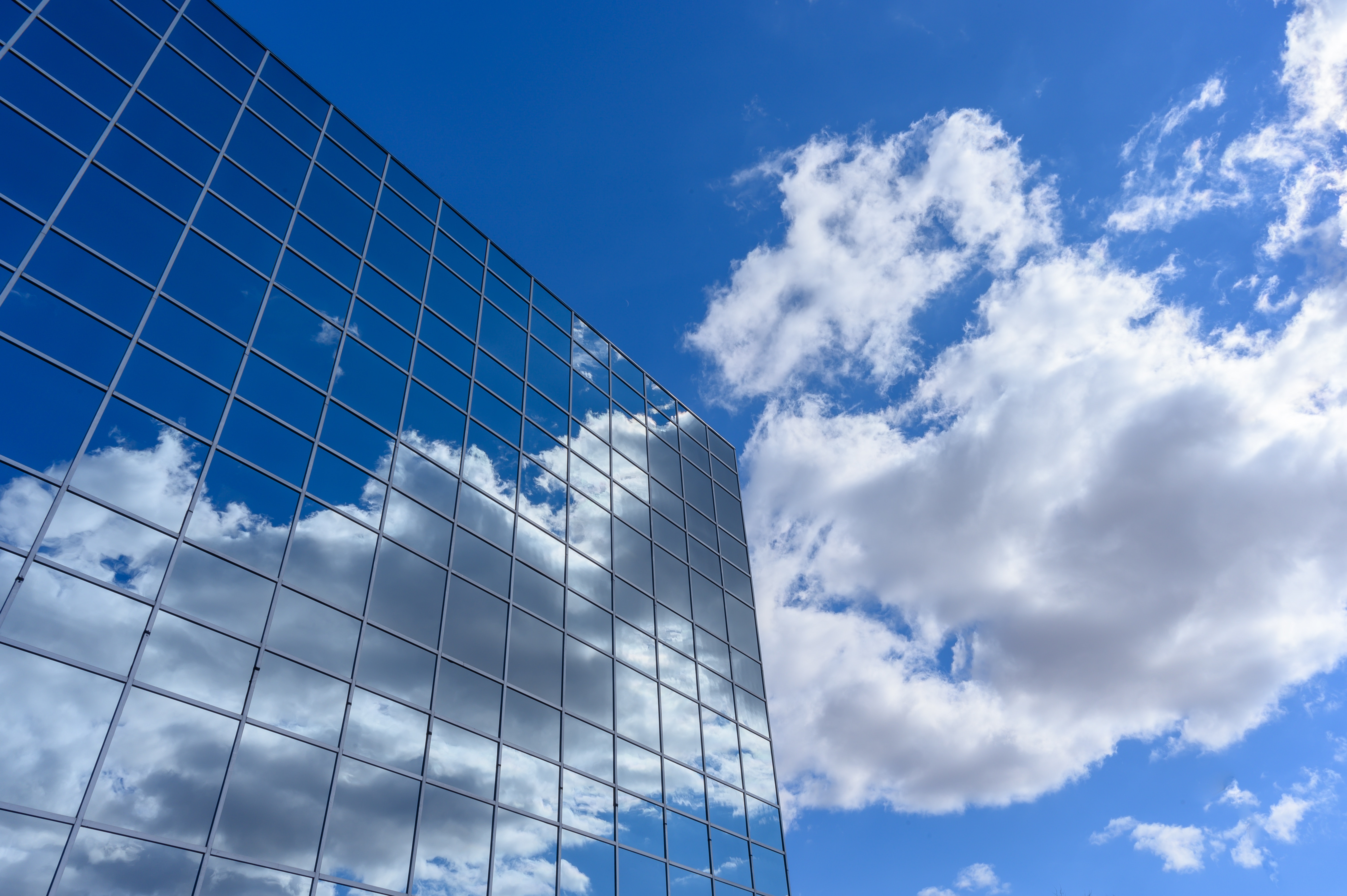 Glasfassade spiegelt blauen Himmel mit weißen Wolken, Himmel rechts sichtbar