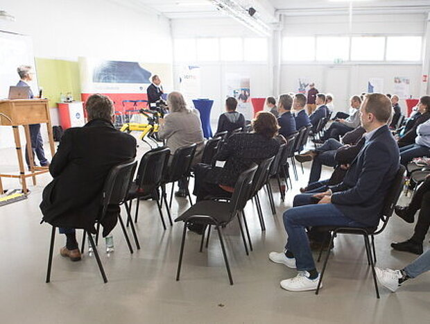 Mehrere Personen sitzen in einer großen Halle und hören einem Vortrag zu