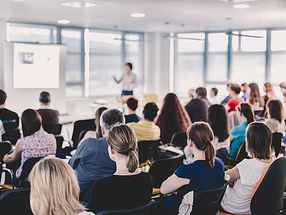 Mehrere Personen verfolgen aufmerksam ein Seminar in einem großen Raum