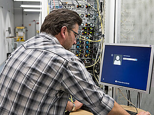 Techniker vor Serverschrank Ein Mann im karierten Hemd steht vor dem Serverschrank und meldet sich an seinem PC an