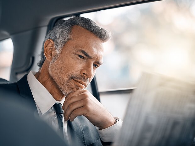 Ein Mann im Anzug sitzt im Auto und liest eine Zeitung