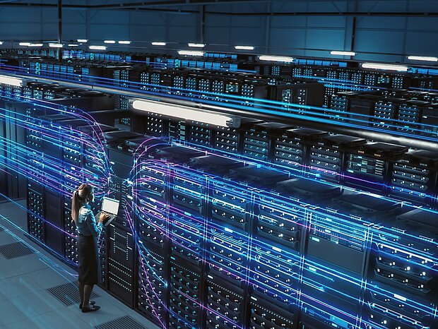 Blick von einer erhöhten position auf einen Serverraum. Zusehen sind mehreren Reihen an blau leuchtenden Server-Schränken.