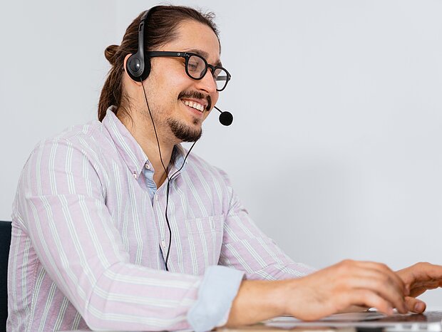 Mann mit Pferdeschwanz und Headset tipp auf einer Tastatur