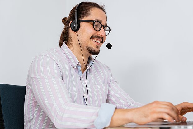 Mann mit Pferdeschwanz und Headset tipp auf einer Tastatur