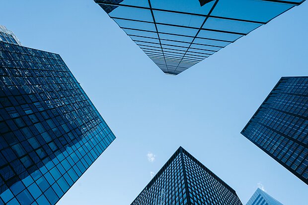 Vier Gebäude spiegeln sich in extremer Perspektive im blauen Himmel.