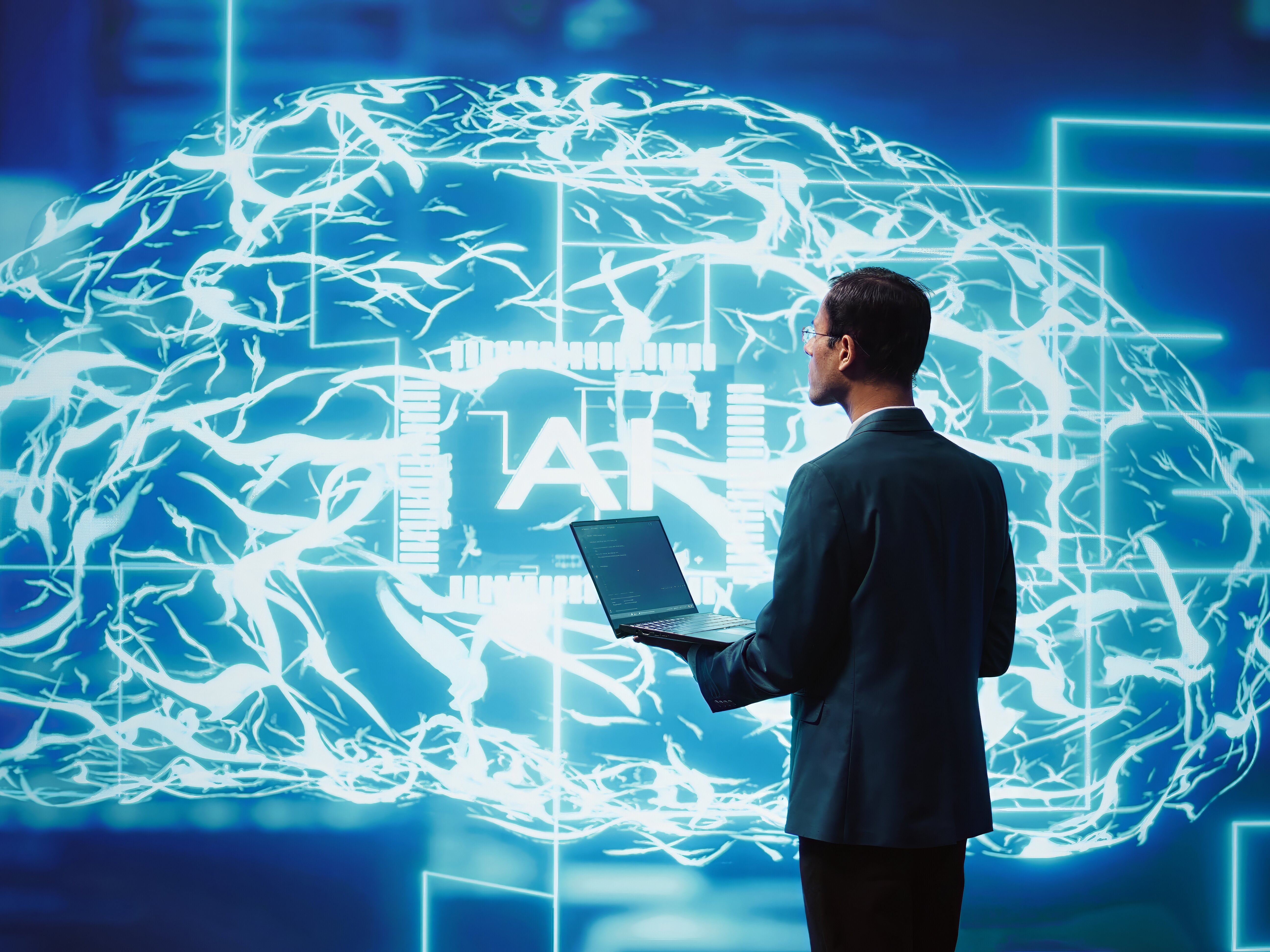 Ein Man mit einem Laptop in der Hand, vor einem digitalem Gehirn. 