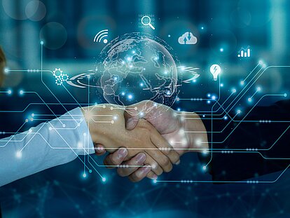 Im Vordergrund erstreckt sich eine transparente Welt als Darstellung von IT-Outsourcing, umgeben von Dienstleistungen. Im Hintergrund reichen sich eine Frau und ein Mann die Hände.